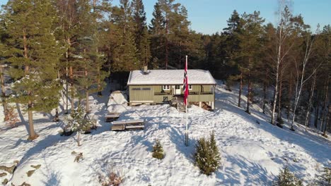 Bandera-Fuera-De-La-Cabaña-Noruega-Con-Un-Bosque-Frondoso-En-El-Fondo-Durante-La-Temporada-De-Invierno-En-Noruega