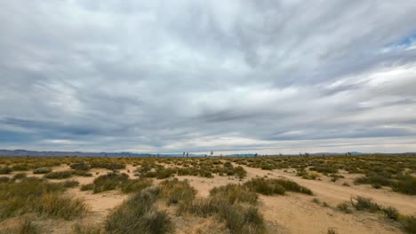 An-overcast-sky-in-the-Mojave-Desert-flows-towards-the-mountains-in-this-daytime,-wide-angle-time-lapse-with-Joshua-trees-and-mountains-in-the-background