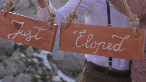 just-eloped-couple-hold-wooden-sings-in-hands-on-mountain-elopement,-closeup
