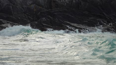 A-close-up-shot-of-the-waves-crashing-on-the-rocks-and-spilling-on-the-sandy-shore
