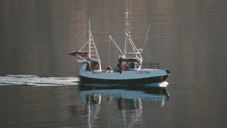 A-small-fishing-ship-moving-slowly-in-the-still-fjord-waters-leaving-the-water-trail-in-its'-wake