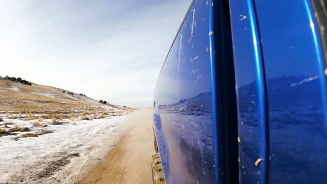 Driving-along-the-historic-Pony-Express-trail-on-a-dirt-road-in-winter---rear-view-from-the-side-of-a-trunk-hyper-lapse