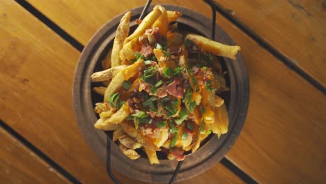 A-stationary-top-down-wide-angle-shot-of-a-full-bowl-of-bacon-and-french-fries-coated-with-cheddar-cheese-and-topped-with-spring-onions