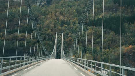 Driving-on-the-narrow-suspension-bridge-above-the-Hardanger-fjord-and-towards-forest-covered-mountains