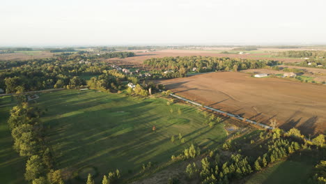 Aerial-Countryside-Landscape-View-in-Pelham-Ontario-Canada-in-Autumn-Season,-Rural-Road-and-Car-Passing-Surrounded-by-Vast-Green-Golf-Field-Farmlands-and-Agricultural-Lands,-Skyline-in-Horizon