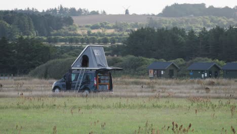 A-custom-built-camper-van-with-an-open-tent-on-the-roof-is-parked-in-the-field