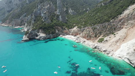 Aerial-drone-video-of-tropical-paradise-turquoise-beach-and-sea-cliffs-in-the-mediterranean,-Cala-Goloritzè,-with-boats