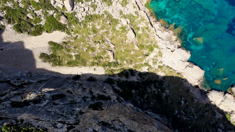 Top-down-aerial-over-sheer-cliff-next-to-brilliant-blue-Balearic-Sea,-Majorca