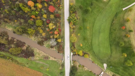 Car-Driving-Moving-Along-Straight-Rural-Countryside-Road-in-Autumn-Season,-Path-Through-Green-Fields-Lands-Trees-and-Country-Homes,-Aerial-Top-Down-Tracking-View