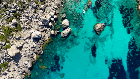 Boat-floats-in-blue-crystal-clear-Mediterranean-water-on-rocky-coast