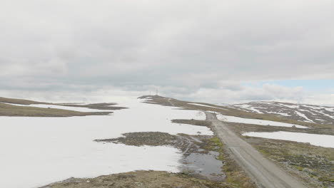 Camino-De-Tierra-Remoto-En-Las-Tierras-Altas-De-Noruega-Con-Nieve-Derretida-En-Un-Día-Nublado,-Aéreo