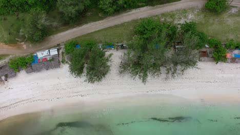 dirt-road-along-white-sand-beach-coastline-with-tropical-turquoise-water-in-Indonesia,-aerial-top-down