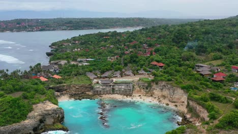hotel-on-a-cliff-at-tropical-Blue-Lagoon-with-turquoise-waves-crashing-on-rocky-beach,-aerial
