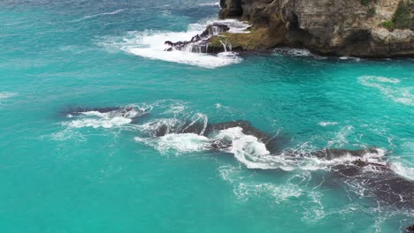 turquoise-tropical-water-crashing-on-jagged-rocks-at-Blue-Lagoon-in-Nusa-Ceningan-Island,-aerial