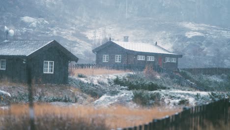 Leichter-Erster-Schnee-Fällt-Auf-Das-Verwelkte-Gras,-Die-Steine-Und-Die-Dächer-Der-Holzhütten-In-Bovertun,-Norwegen