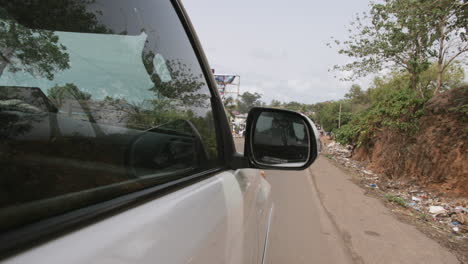 Slow-motion-footage-focused-on-the-rearview-side-mirror-of-a-vehicle-driving-down-the-road-in-Africa