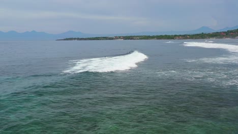 surfers-in-the-ocean-as-waves-break-onto-the-coastline-in-Nusa-Ceningan-Bali,-aerial