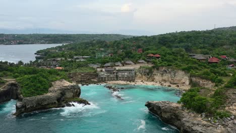 aerial-of-rocky-cliffs-at-blue-lagoon-in-Nusa-Ceningan-on-cloudy-afternoon-sunset