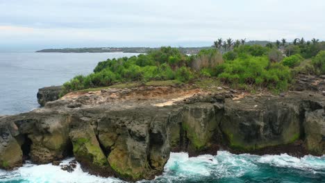 dangerous-waves-and-cliffs-at-Nusa-Ceningan-Island-on-cloudy-day,-aerial