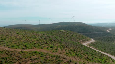 Drone-flyover-Mountain-road-leading-windmills-on-forested-hilltop,-Scenic-Landscape,-Chile