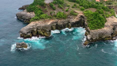 turquoise-blue-tropical-water-crashing-onto-the-cliffs-at-Nusa-Ceningan-Island-in-Indonesia,-aerial