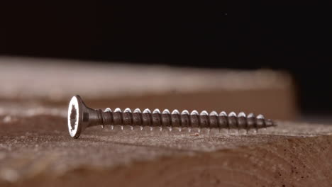 Long-Metal-Screw-Fall-On-Wooden-Board-With-Blurry-Background