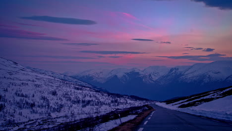 Static-shot-of-winding-road-through-winter-mountains-during-evening-time-in-timelapse