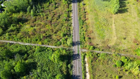 Forward-aerial-reveal-of-train-tracks-through-forest-by-water,-Canada