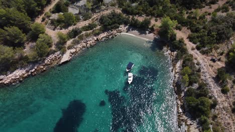 Cinematic-orbit-shot-of-a-secluded-private-beach-on-Brac-Island,-Croatia-with-two-boats-anchored-on-the-turquoise-water-of-Adriatic-Sea