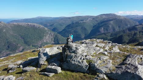 Aerial-orbiting-slowly-around-man-standing-on-Stamneshella-mountaintop-in-Norway-with-Bolstadfjorden-deep-down-below-and-surrounded-by-spectacular-mountain-scenery