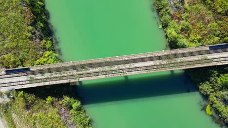 Rising-spinning-overhead-aerial-of-train-tracks-over-green-water-river
