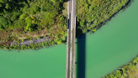 Top-down-shot-of-grassy-abandoned-railway-track-on-bridge-over-calm-clean-river