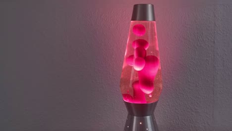 Several-warm,-red-bubbles-rising-and-falling-inside-a-retro-lava-lamp-in-front-of-white-interior-wall