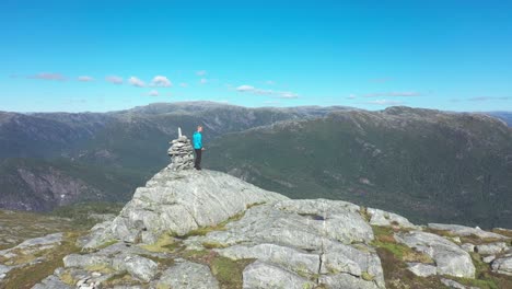 Man-standing-on-top-of-mountain-and-enjoying-beautiful-Norwegian-mountain-scenery---Forward-moving-aerial-passing-close-to-man-and-continuing-forward-into-vast-landscape---Stamneshella-Bolstadfjord