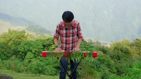 A-stationary-footage-of-a-man,-playing-his-electronic-musical-keyboard-passionately-in-the-forest-near-the-mountains