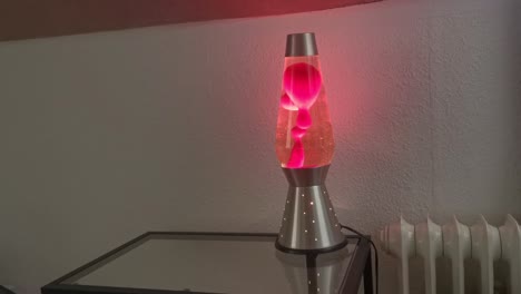 Glowing,-bubbling-lava-lamp-standing-on-a-glass-table-next-to-a-wall-mounted-radiator