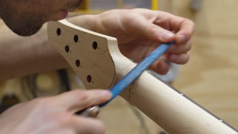 Close-up-view-of-a-young-luthier-shaping-guitar's-neck-with-rasp,-removing-roughness-and-bumps