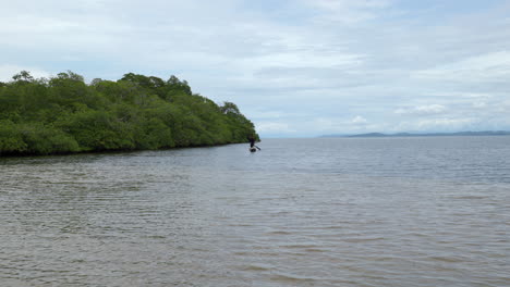 Static-far-away-shot-of-a-local-Panamanian-rowing-in-a-small-boat-looking-for-fish-in-the-water-near-the-jungle
