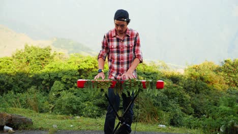 A-stationary-footage-of-a-man,-playing-his-electronic-musical-keyboard-in-the-forest-near-the-mountains