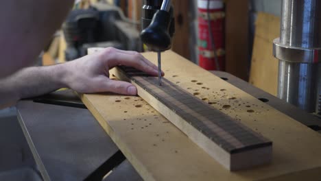 Luthier's-hands-drilling-holes-in-fretboard-for-fretmarkers-with-drill-press-machine