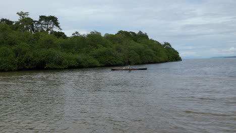 Static-shot-of-a-local-Panamanian-rowing-in-a-small-boat-looking-for-fish-in-the-water-near-the-jungle