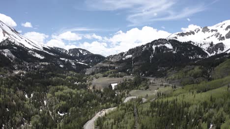 Montañas-Rocosas-De-Colorado-Con-Picos-Nevados-Y-Camino-Que-Conduce-A-Un-Despeje,-Tiro-Aéreo
