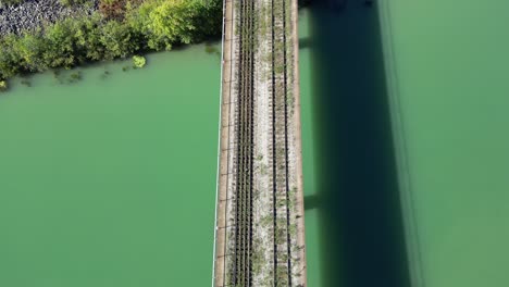 Endless-abandoned-railway-track-on-bridge-over-river-heading-into-forest,-aerial