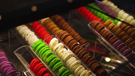 View-into-glass-display-case-of-colorful-macarons-in-dimly-lit,-high-end-bakery