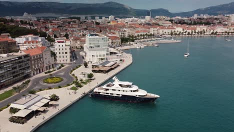 Aerial-orbit-shot-of-a-beautiful-yacht-parked-at-the-port-of-Split,-Croatia-alongsite-the-coastline-of-Adriatic-sea-and-croatian-mountains