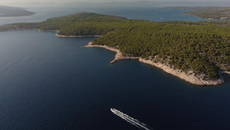 Aerial-panning-shot-of-a-high-speed-boat-cruising-along-the-coastline-of-Brac-Island,-Croatia,-navigating-between-Hvar-and-Milna-over-the-Adriatic-Sea