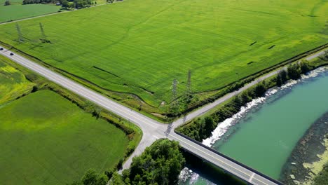 Flat-rural-plot-of-land-with-corn-farm-along-river-with-power-lines,-aerial