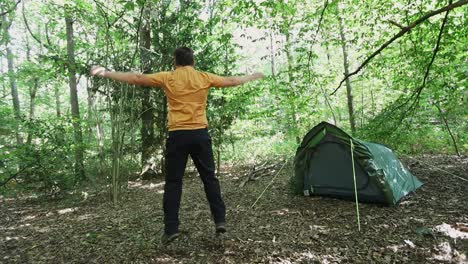 Young-man-doing-jumping-jacks-in-forest-campsite,-slow-motion-view-from-the-back