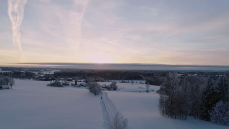 Aerial-shot-of-vivid-sunset-sky-over-snow-covered-woodland-landscape---stunning-white-winter-scenery