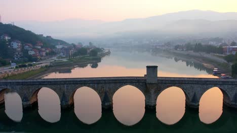 Sunrise-aerial-of-person-walking-over-bridge-drina-river-in-Visegrad,-Bosnia,
